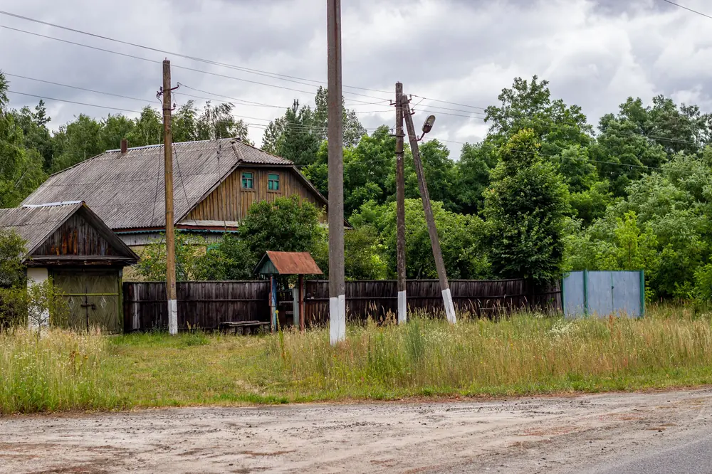 Селска улица с дървена къща, ограда и електрически стълбове